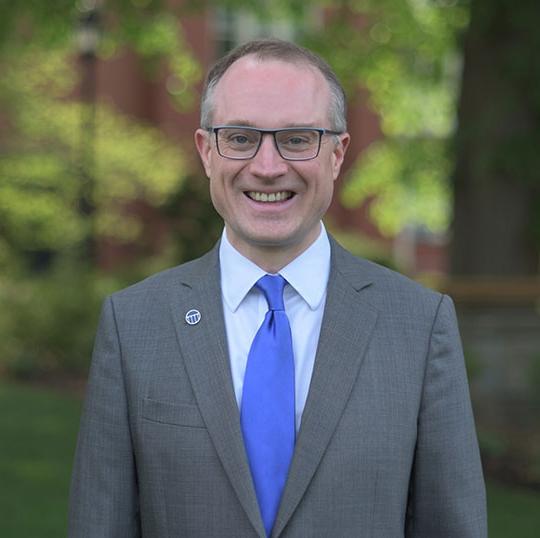 headshot of man in suit 和 tie, wearing glasses